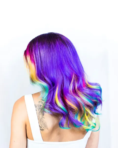 Lange violette Haare von hinten, die Spitzen laufen in Pink, Gelb und Türkis aus.